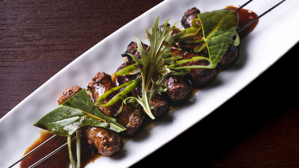 Spiedo di salsiccia di suino nero, tamarindo, cipollotto, togarashi. Sausage skewer with black pork sausage, tamarind, scallion, togarashi